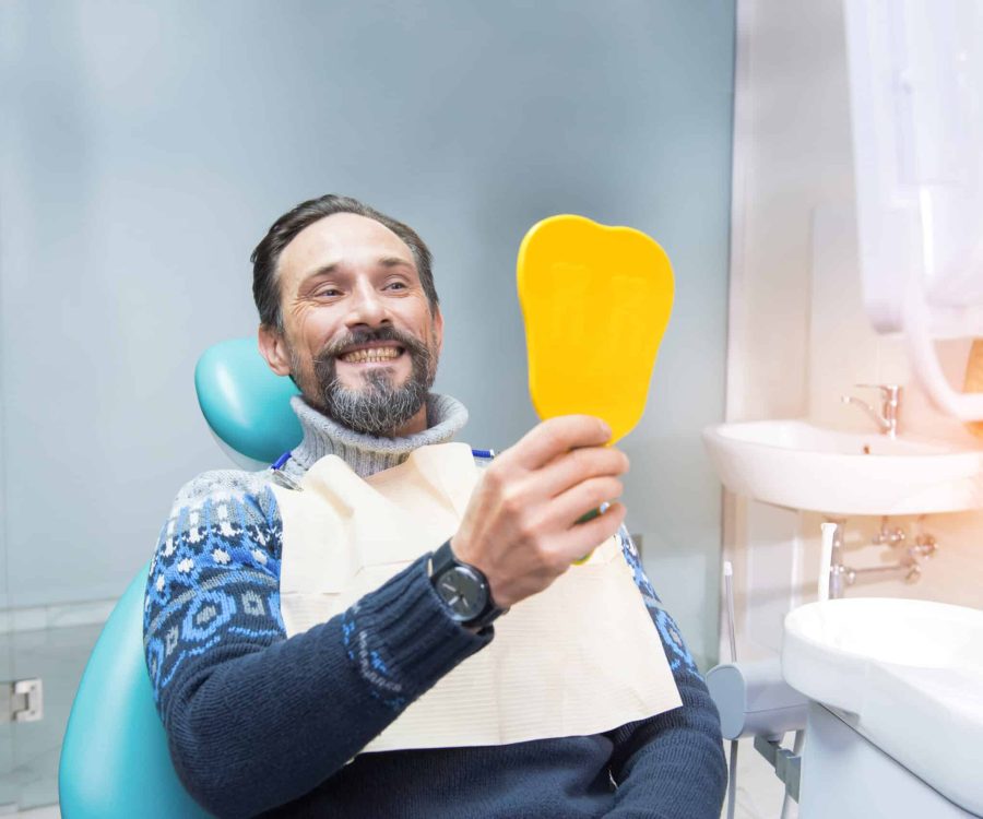 Man in dental chair. Person holding mirror and smiling. Fix your smile.